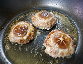 フライパンに油を引き、丸く成形した肉だねを並べ椎茸を乗せる様子。